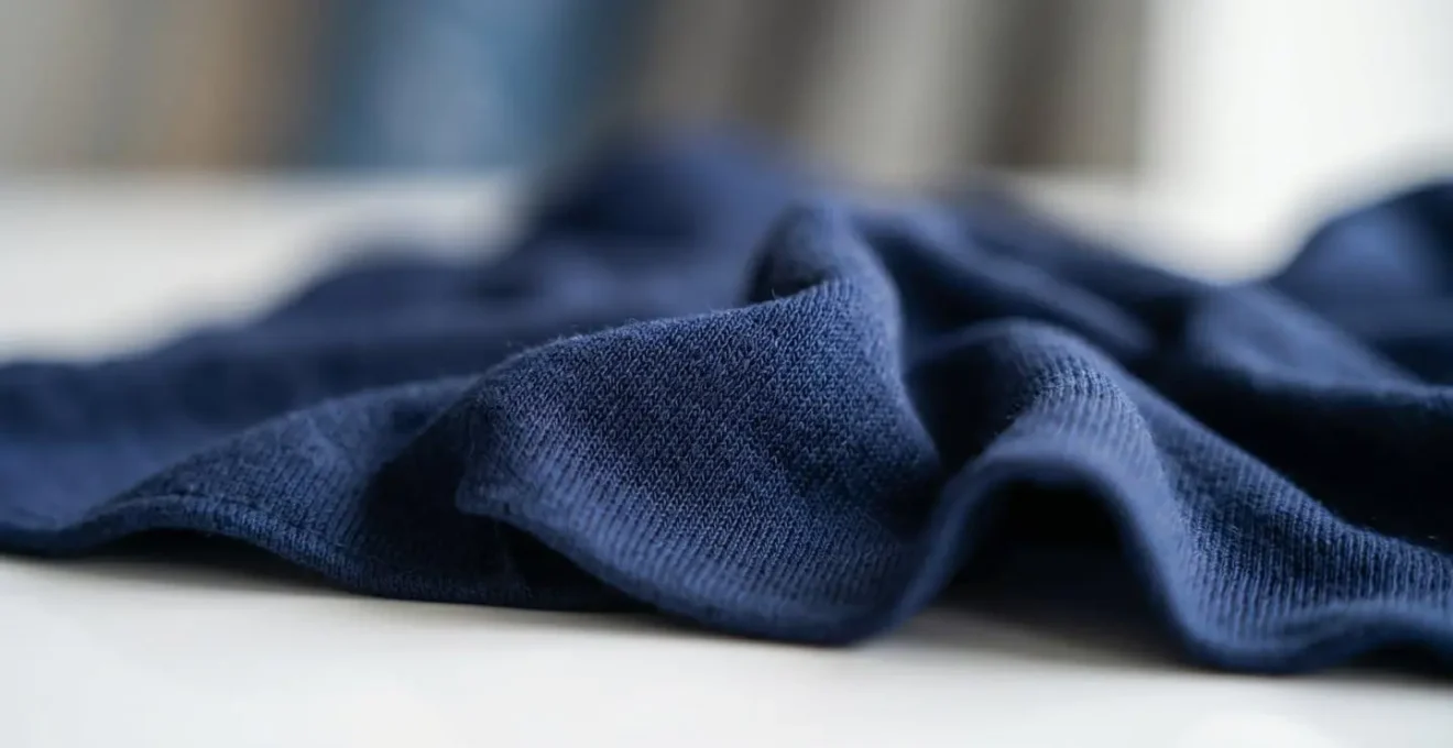 Gros plan sur la texture d'un hijab en jersey liquid avec des plis naturels et des reflets de lumière sur une surface blanche épurée